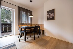 Un coin repas comprenant une table, des chaises, un luminaire suspendu, une fenêtre avec des rideaux et un tableau encadré au mur.