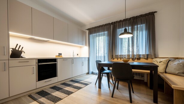 A modern kitchen with built-in appliances, a dining area with a bench, and a large window with curtains. - Apartment 'Plose 35' in strategic location with Mountain View, Balcony & Wi-Fi (Bressanone)