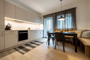 Eine moderne Küche mit integrierten Geräten, ein Essbereich mit einer Bank und ein großes Fenster mit Vorhängen.