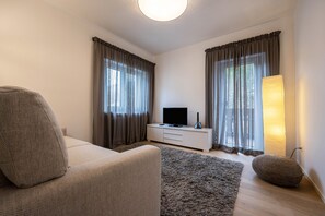 Un salon moderne avec un canapé, un téléviseur à écran plat, un meuble blanc et une lampe.