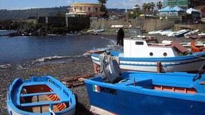 A coastal area with boats docked near the shore, a building with a clock tower, and a rocky beach. - Sicily new apartment next sea with two bedrooms (Acireale)
