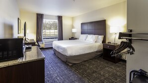 A hotel room with a bed, a desk, a chair, a TV, a lamp, a coat rack, and a window with curtains. - Cobblestone Inn & Suites - Springfield (Springfield)