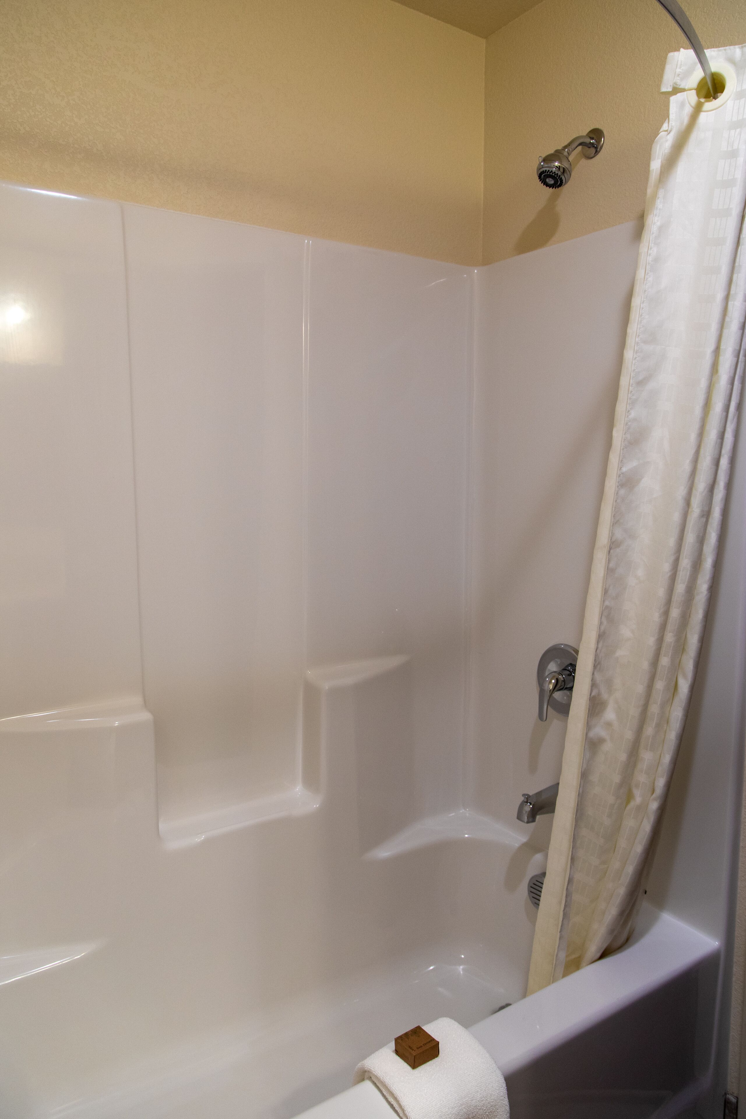 A white bathtub with a showerhead, a towel, and a curtain.