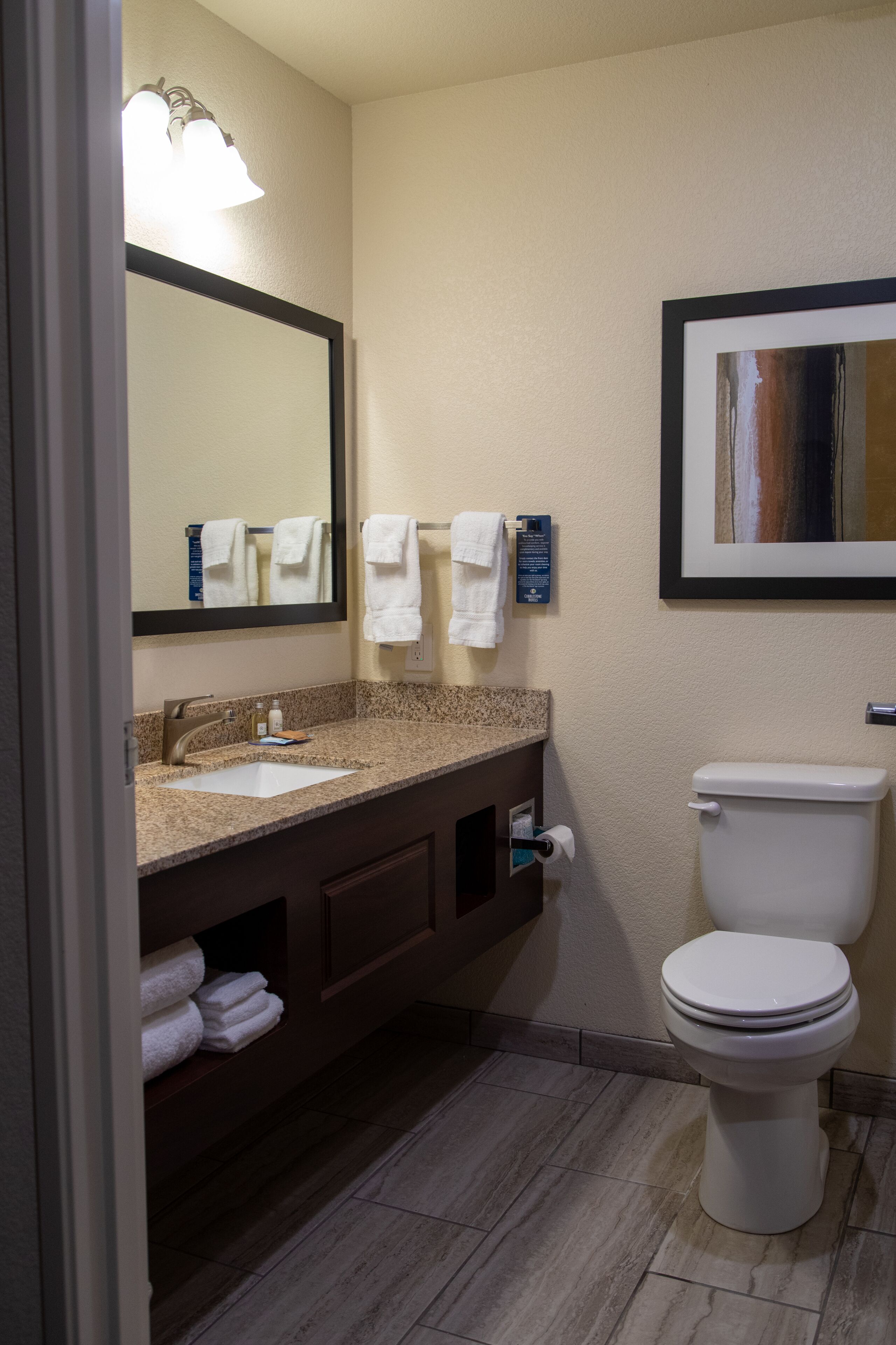 Un baño de hotel con lavamanos, espejo, toallero y retrete.