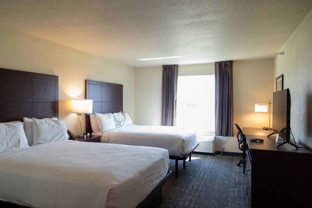 A hotel room with two beds, a desk, a chair, a TV, and a window with curtains.