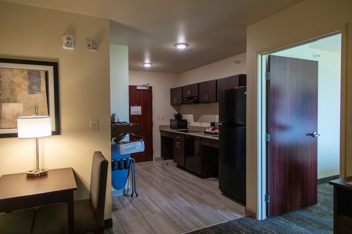 A compact kitchen with dark wooden cabinets, a black refrigerator, and a blue laundry cart.