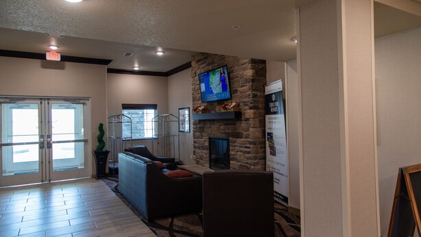 A modern lobby with a stone fireplace, comfortable seating, a large TV screen, and a glass door entrance. - Cobblestone Inn & Suites - Springfield (Springfield)