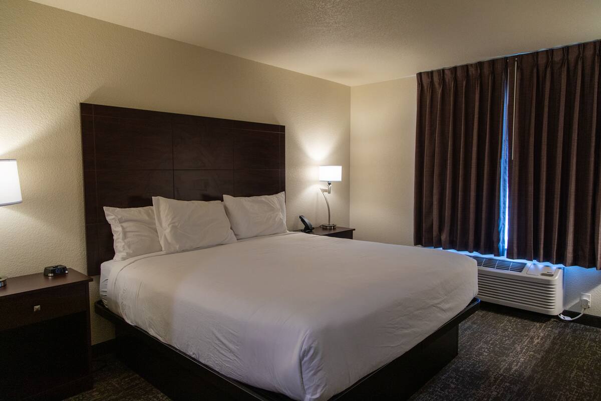 A hotel room with a large bed, a nightstand with a lamp, a heater, and a window with curtains.