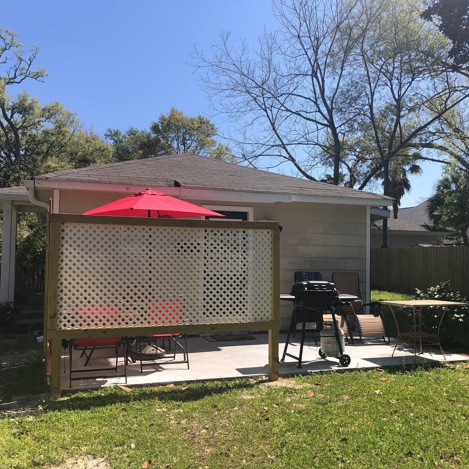 Un pati amb zona de terrassa, una barbacoa i una zona de seients coberta amb un parasol vermell.