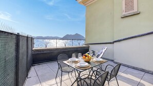 Un balcon avec une table dressée pour deux personnes, un panier de fruits et une vue sur les montagnes.
