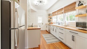 Una cocina moderna con armarios blancos, un refrigerador de acero inoxidable, encimeras de madera y un horno integrado.