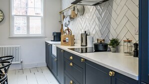 Une cuisine moderne avec un dosseret de carreaux disposés en motif chevron, une fenêtre avec des stores et une variété d’ustensiles et d’appareils de cuisine sur le plan de travail.