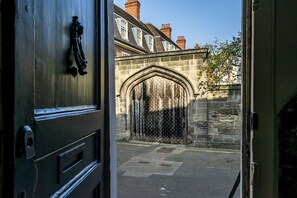 A view through a door into a courtyard with a stone archway and a building with windows in the background.