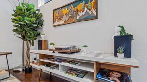 Una sala de estar moderna con una mesa consola blanca, libros, un tocadiscos y un cuadro de montañas.