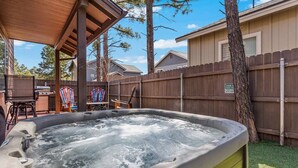 Un jacuzzi en un patio trasero con terraza de madera, una parrilla y un área de estar cubierta.