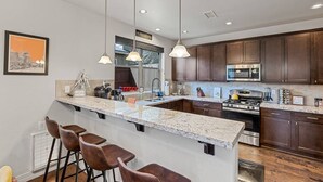 Una cocina moderna con una isla grande, armarios de madera oscura, electrodomésticos de acero inoxidable e iluminación colgante.