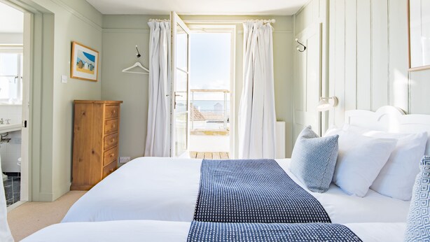 Une chambre à coucher avec un lit, une commode en bois, une fenêtre avec des rideaux et une vue sur l’extérieur.