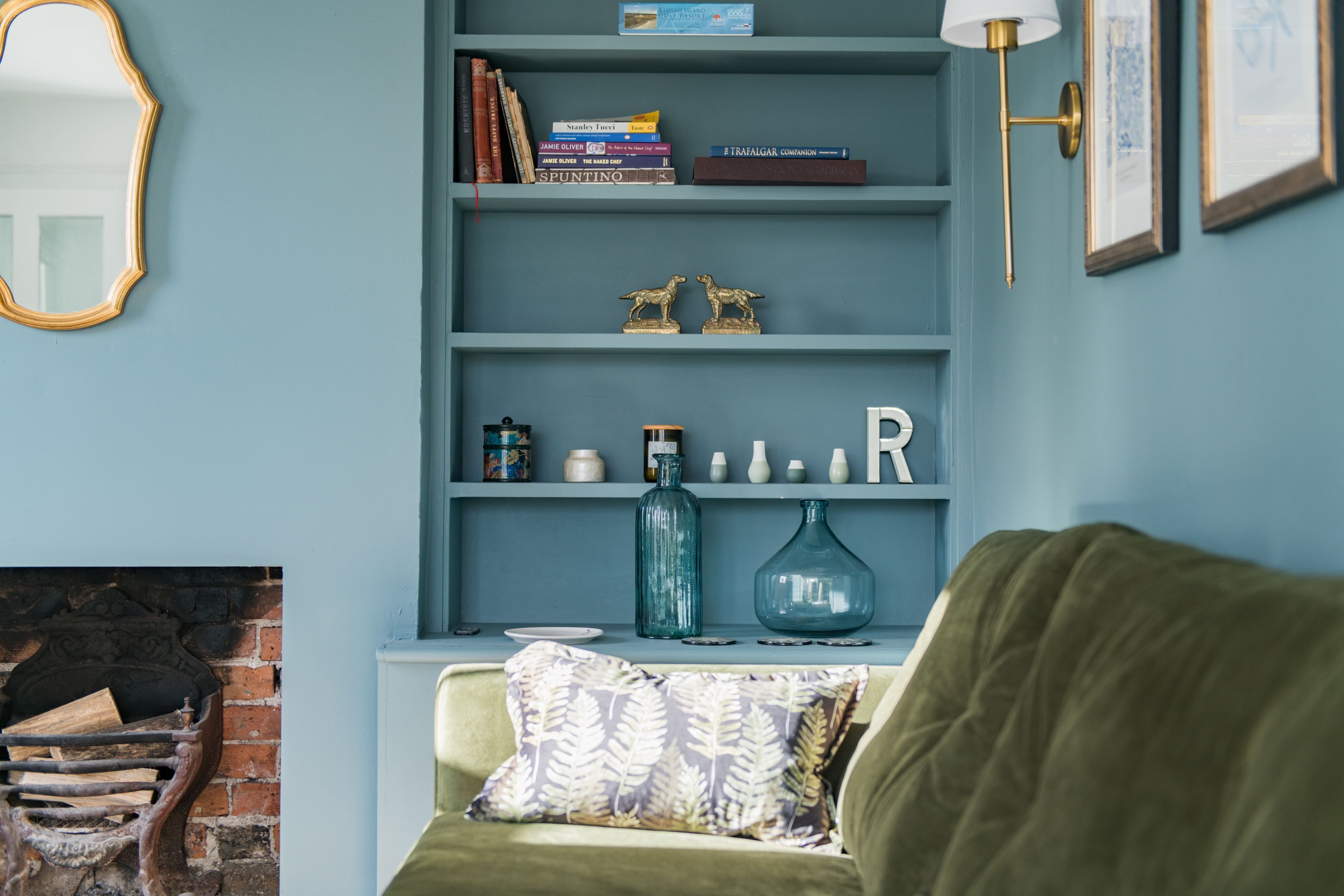 Una habitación con una estantería azul, chimenea y un sofá verde.