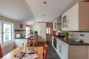 A kitchen with white cabinets, a wooden dining table, and a window. - Charming holiday  cottage in the centre of Deal, sleeping 6 guests, 2 bathrooms seconds from the sea (Deal)