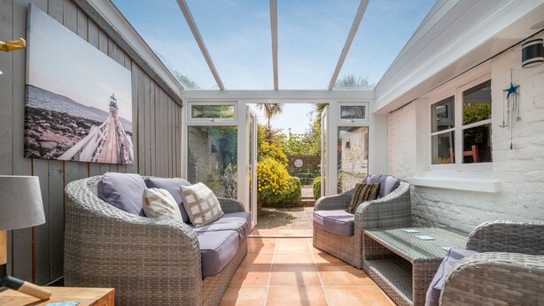 A sunlit patio with wicker furniture, a painting of a lighthouse, and a view of the garden. - Charming holiday  cottage in the centre of Deal, sleeping 6 guests, 2 bathrooms seconds from the sea (Deal)