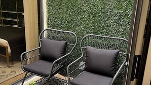 A patio area with two wicker chairs and a small table, a patterned floor, and a wall with 'PALM DESERT' written on it. - Palm Desert Luxury Condo -Country Club (Palm Desert)