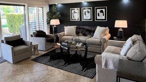 A modern living room with a sofa set, two armchairs, a coffee table, and a black rug. There are three framed pictures on the wall and a potted plant. - Palm Desert Luxury Condo -Country Club (Palm Desert)