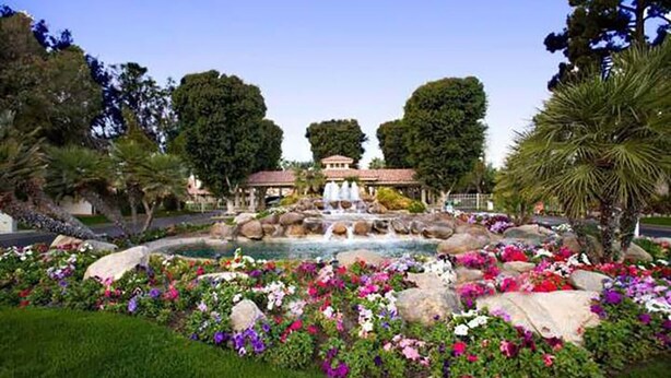 A landscaped garden with a fountain, surrounded by various flowers and trees. - Palm Desert Luxury Condo -Country Club (Palm Desert)