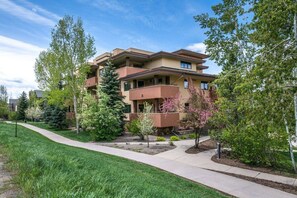A multi-story residential building with a landscaped front yard, a sidewalk, and mature trees.