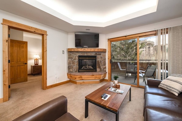 A living room with a stone fireplace, a flat-screen TV, a sofa, a coffee table, and a sliding glass door leading to an outdoor area.