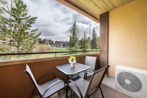 Enjoy a peaceful view from this balcony with a table and chairs, overlooking a building and lawn.