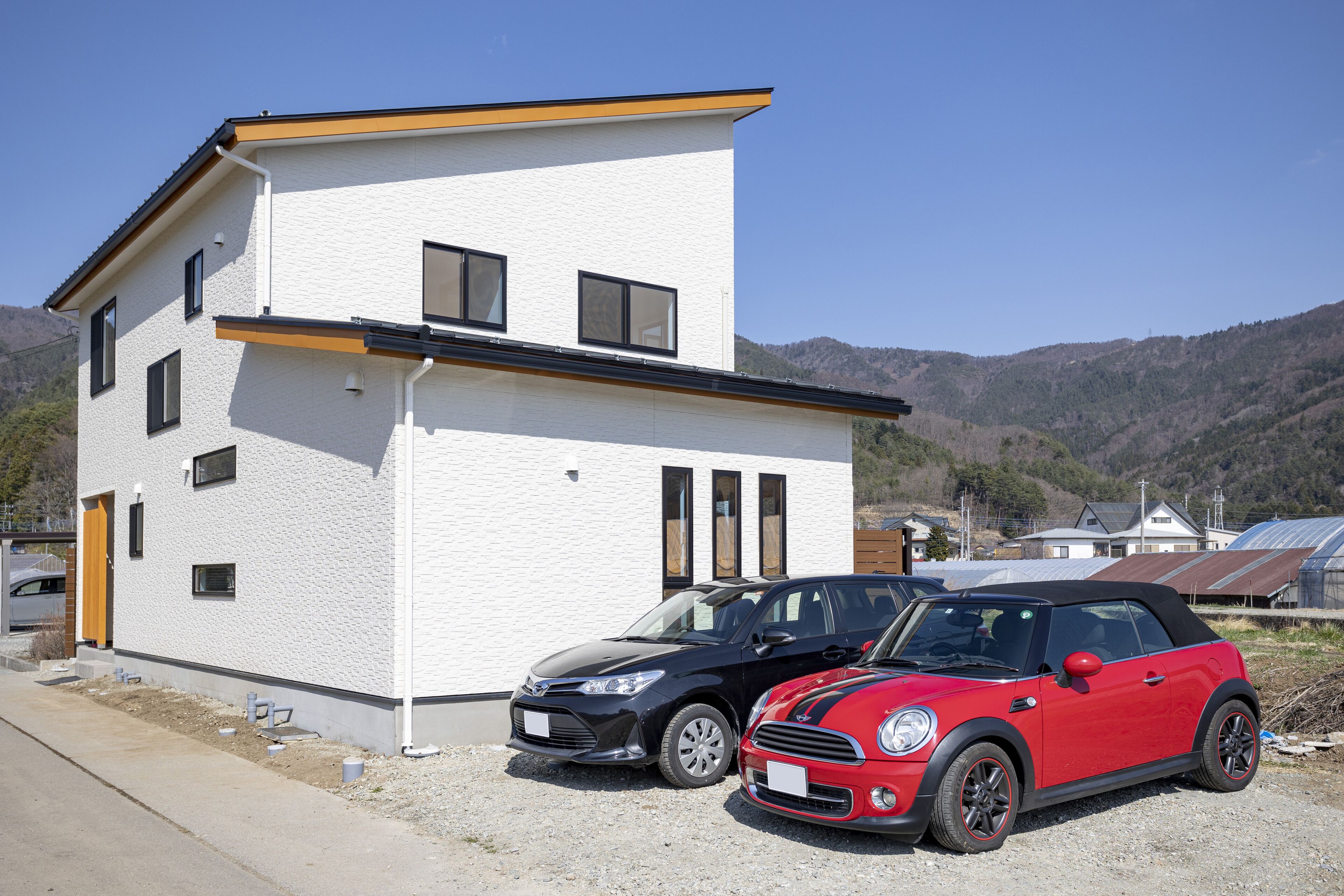 A modern two-story house with a white exterior and black trim. There are two cars parked in front: a black hatchback and a red convertible.