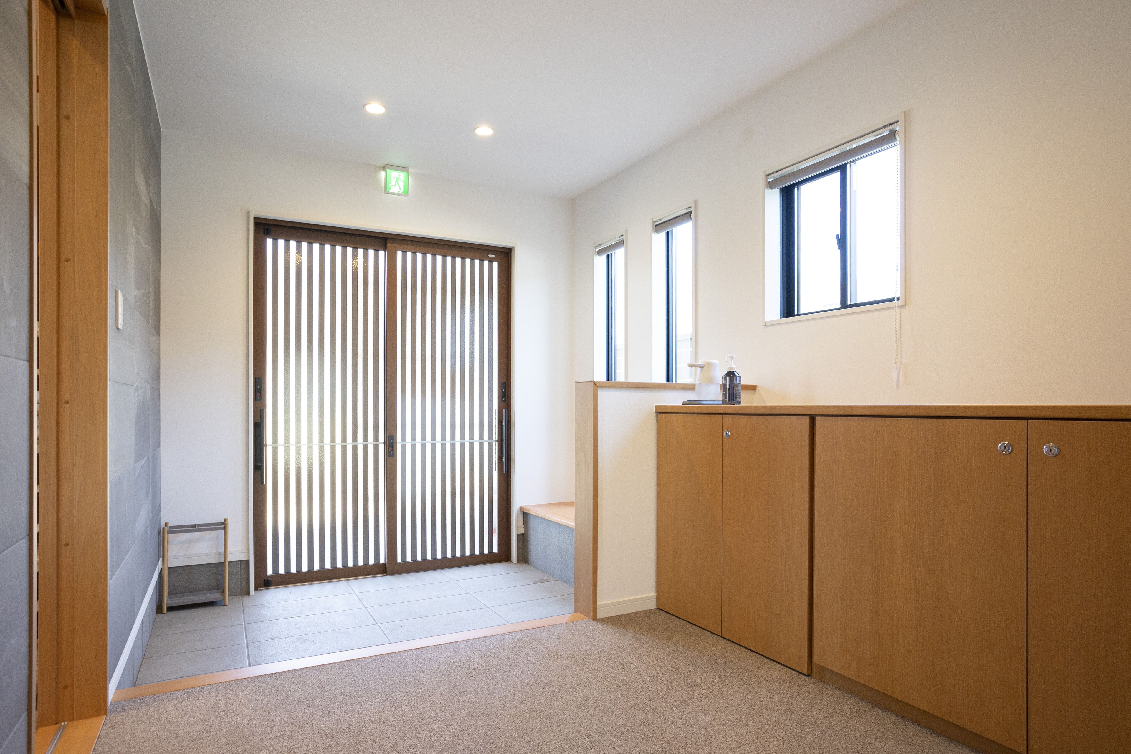 A hallway with a sliding door, a small bench, and a cabinet with a window above it.
