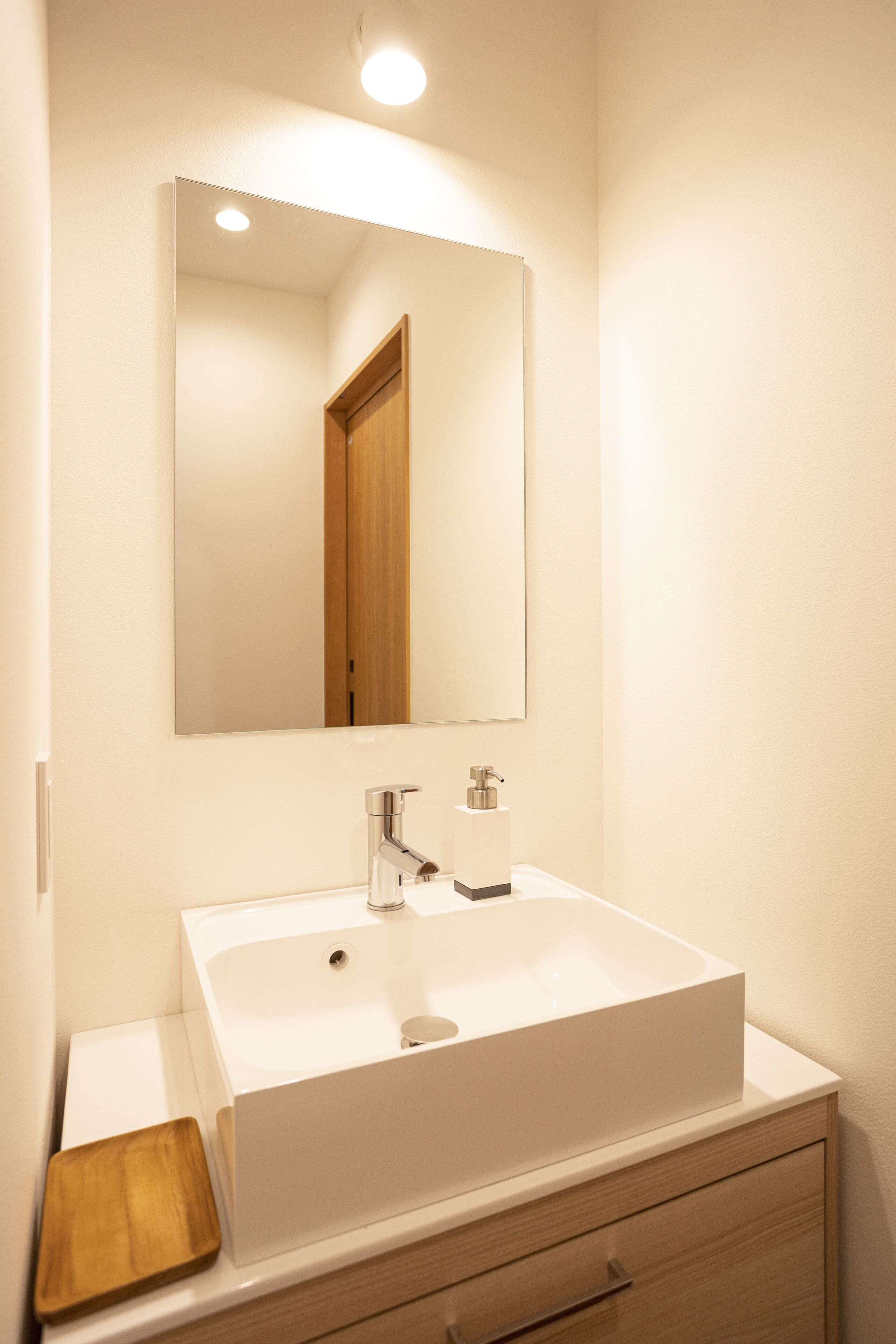 A bathroom with a white sink, a mirror, and a wooden tray.