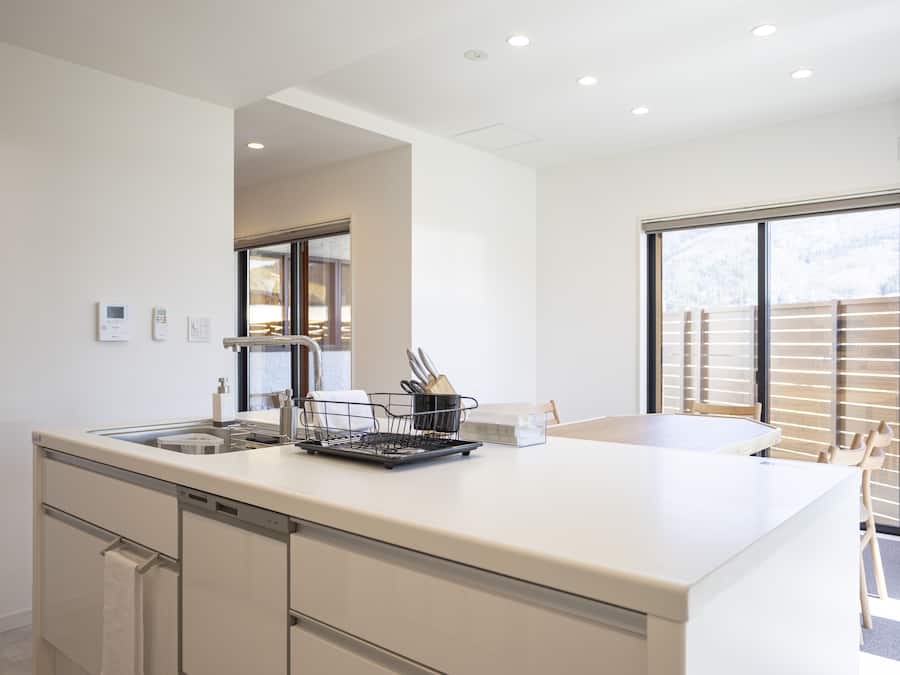 A modern kitchen with a large island, built-in dishwasher, and a window with blinds.