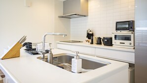 Et moderne køkken med stålvask, hvide bordplader, indbygget mikrobølgeovn og emhætte.
