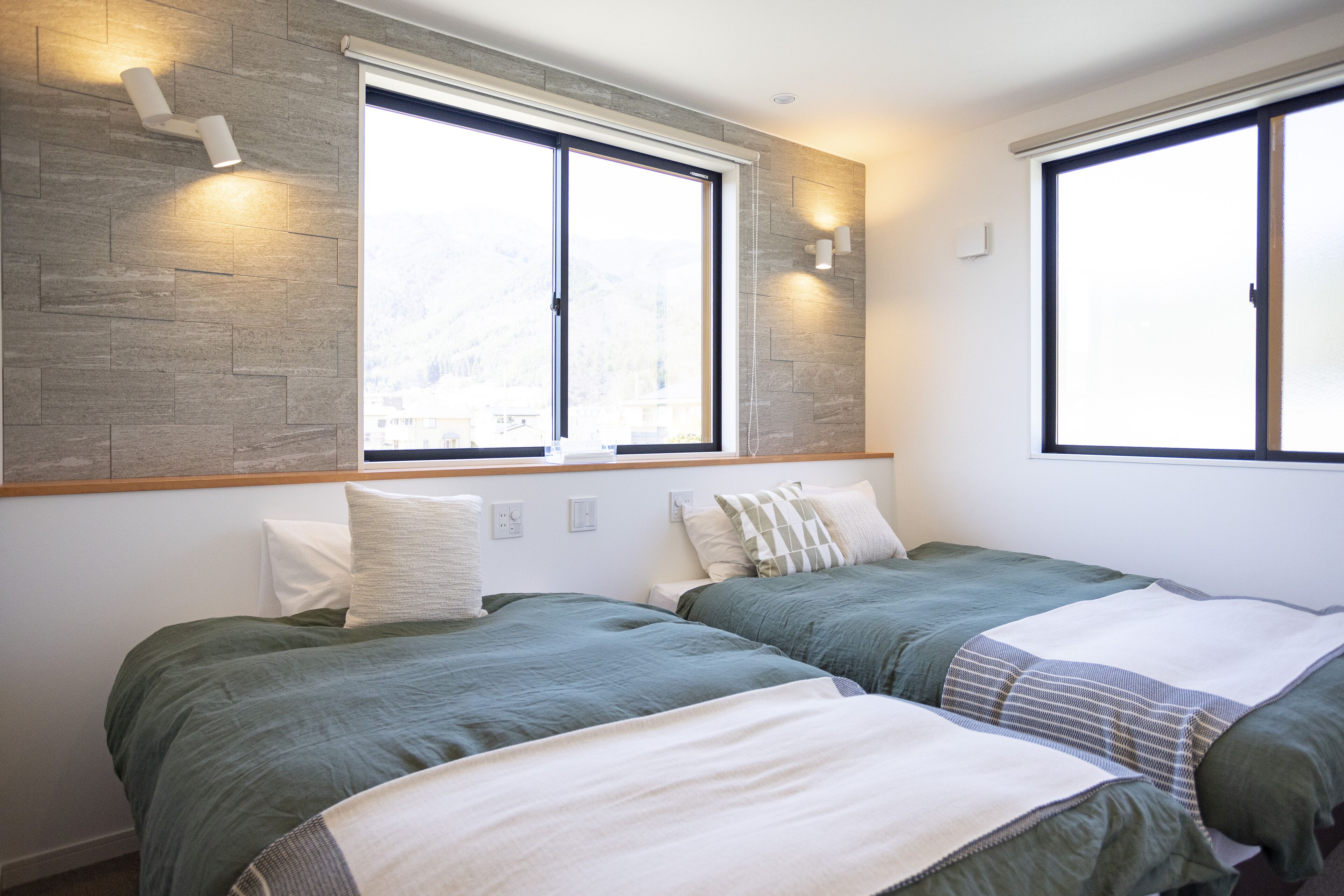 A modern bedroom with two beds, large windows, and built-in lighting.