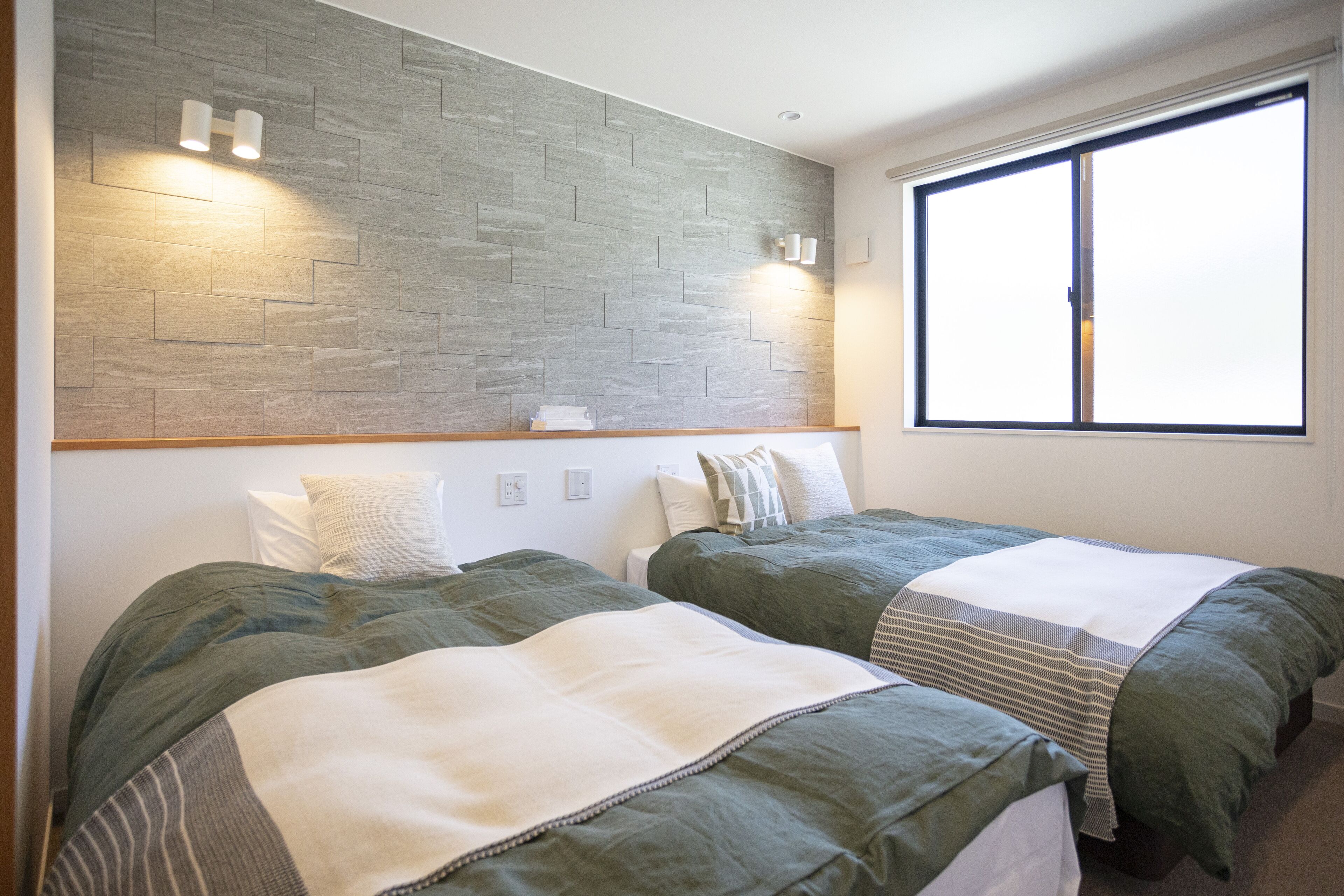 A bedroom with two beds, a herringbone-patterned wall, and a large window.