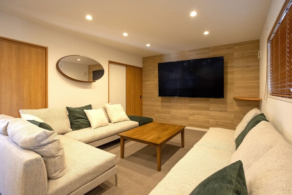 Una sala de estar moderna con un sofá, una mesa de centro, un televisor de pantalla plana montado en la pared y piso de madera.