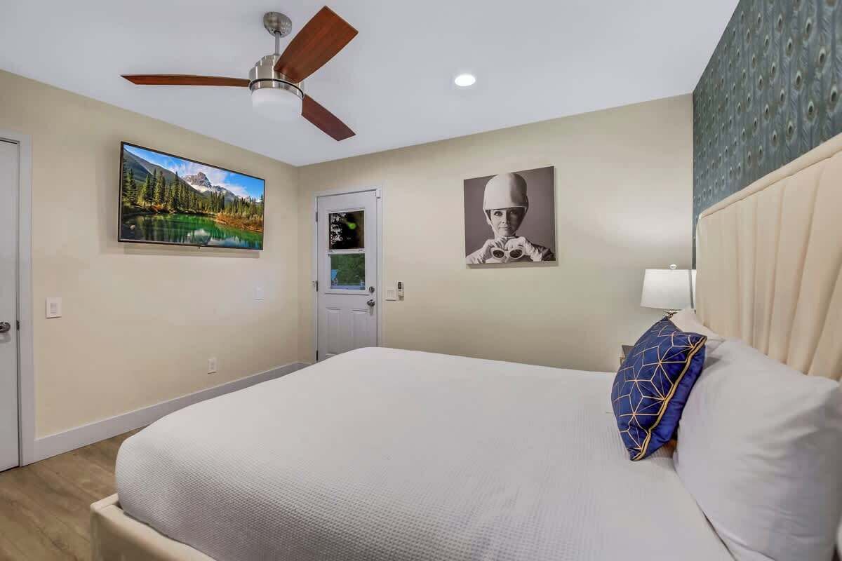 Ein Schlafzimmer mit einem Bett, einem Deckenventilator, einer Tür und zwei gerahmten Bildern an der Wand.