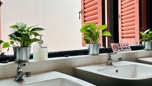 A bathroom with two sinks, a hand soap dispenser, and potted plants. A no-smoking sign is visible on the window sill. - Rucksack Inn Temple Street (Singapore)
