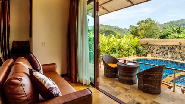 A room with a leather sofa, a glass door leading to a pool area with wicker furniture.