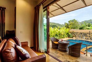 Una habitación con un sofá de cuero, un ventanal que da a una zona de piscina con mobiliario de mimbre.