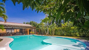 A swimming pool with a curved design, surrounded by lush greenery and a building with outdoor seating. - Prayai Changthai Resort (Chalong)