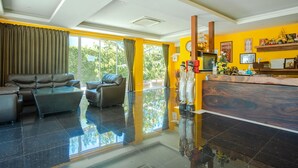 A modern hotel lobby with a sofa, chairs, a reception desk, and a large window offering a view of greenery. - Prayai Changthai Resort (Chalong)