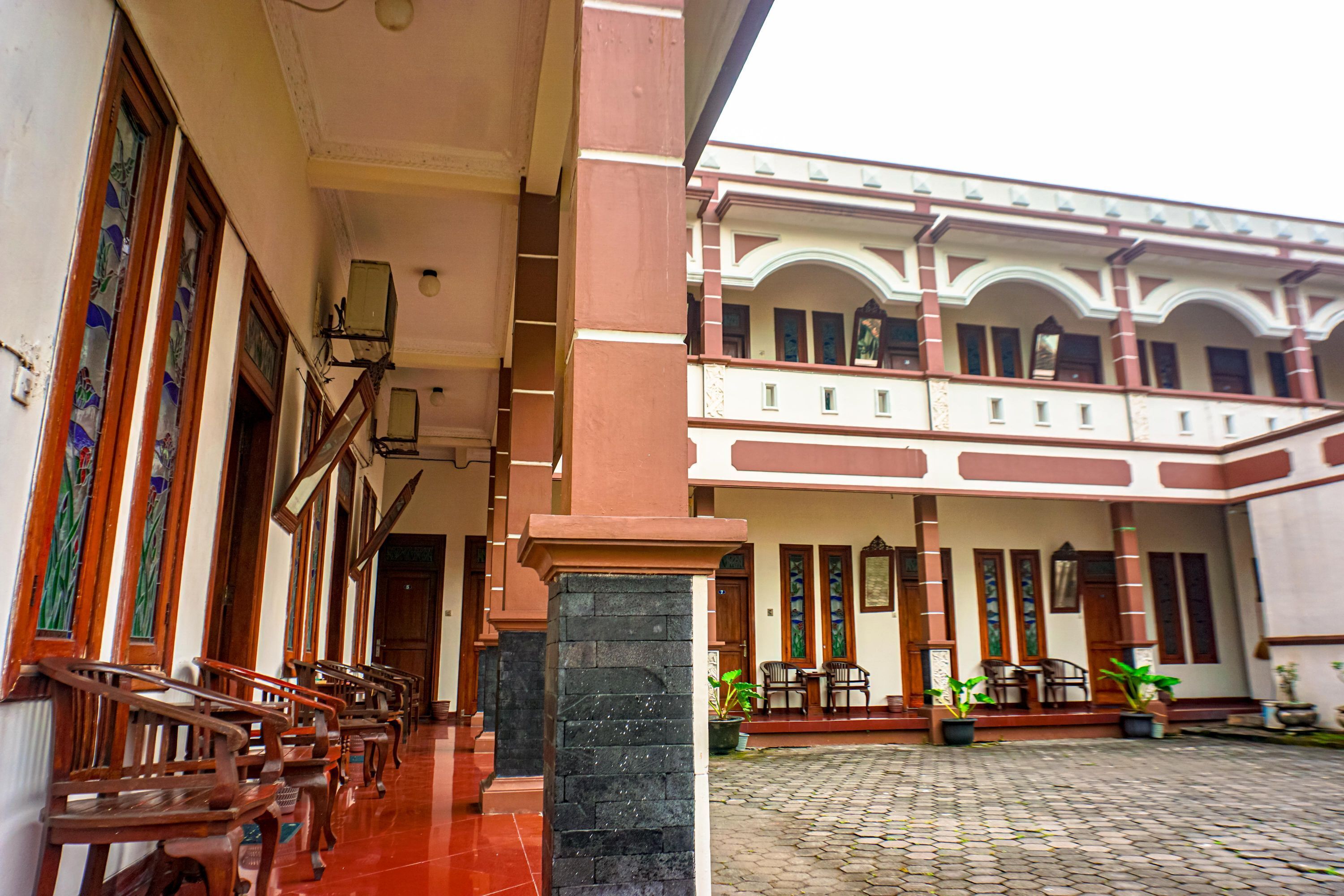 A building with a covered walkway, wooden benches, and potted plants.