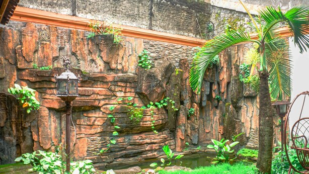 Un mur de pierres rustiques agrémenté d’une petite fontaine et d’un palmier.