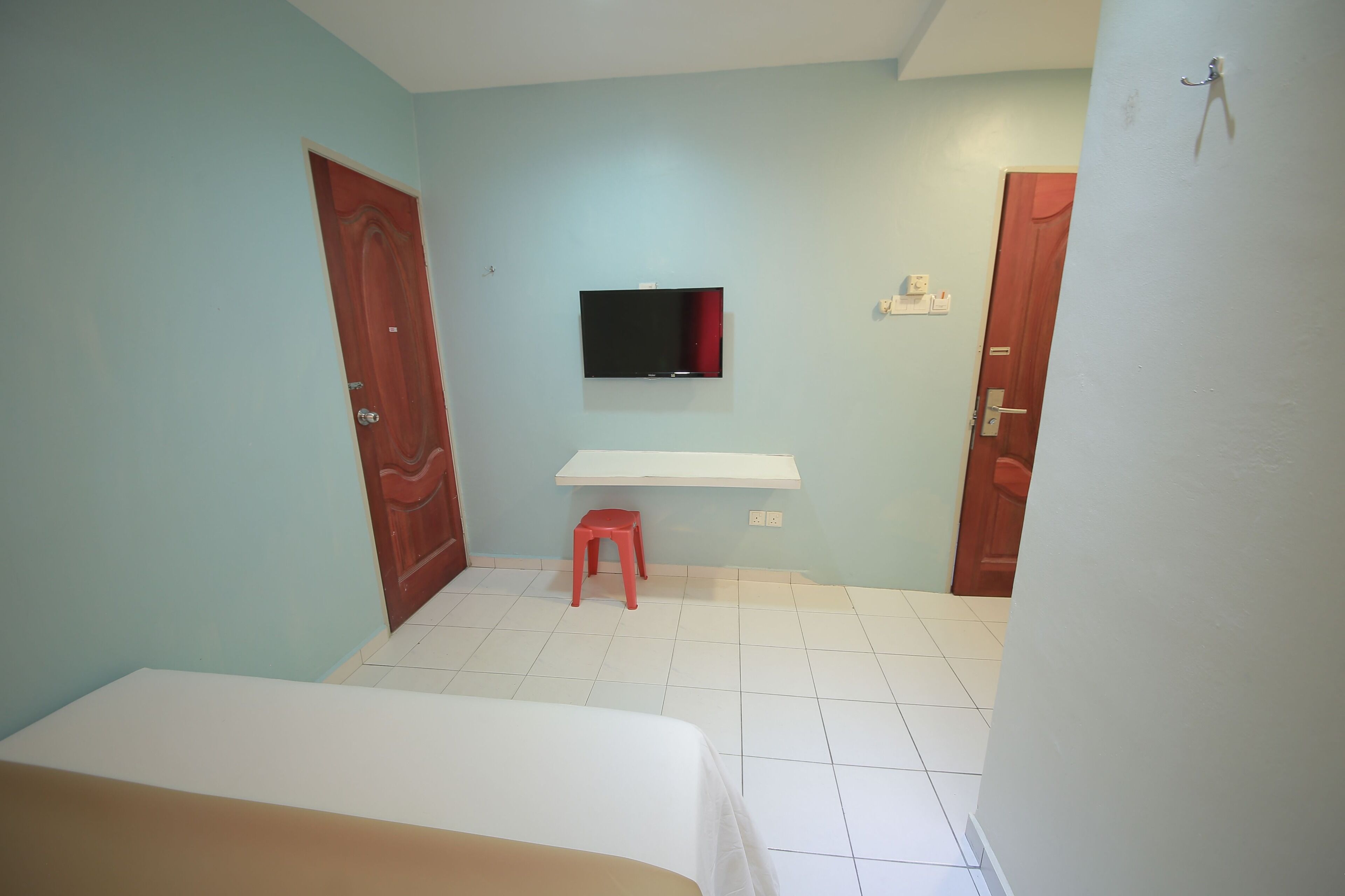 A room with a bed, a TV mounted on the wall, a small stool, and two doors.