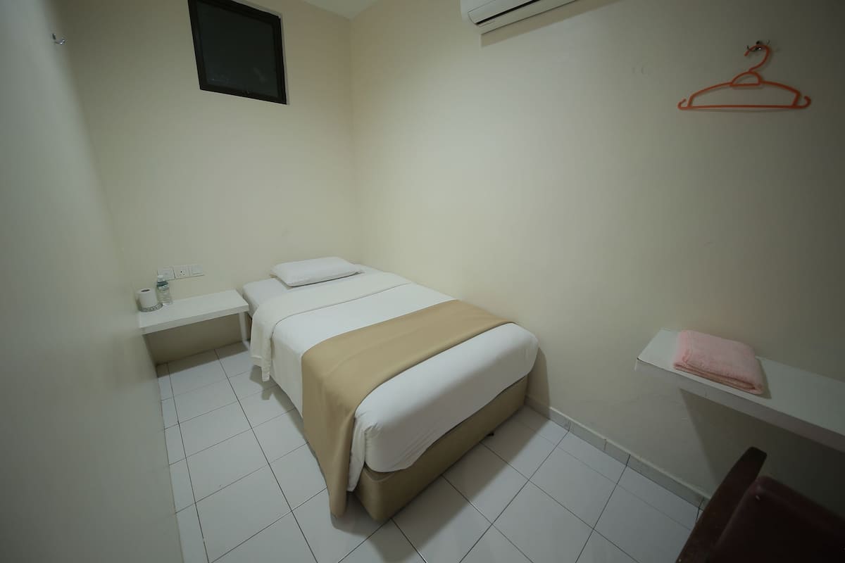 A small, clean room with a bed, a nightstand, a shelf with a towel, and a red hanger on the wall.