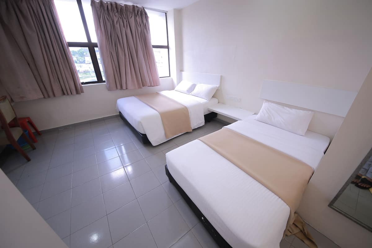A hotel room with two beds, a window with curtains, a small table, and a chair.