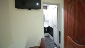 A hallway with a mounted TV, a wooden door, and a bathroom visible through an open door. - Skudai Hotel Universiti Teknologi Malaysia (Johor Bahru)